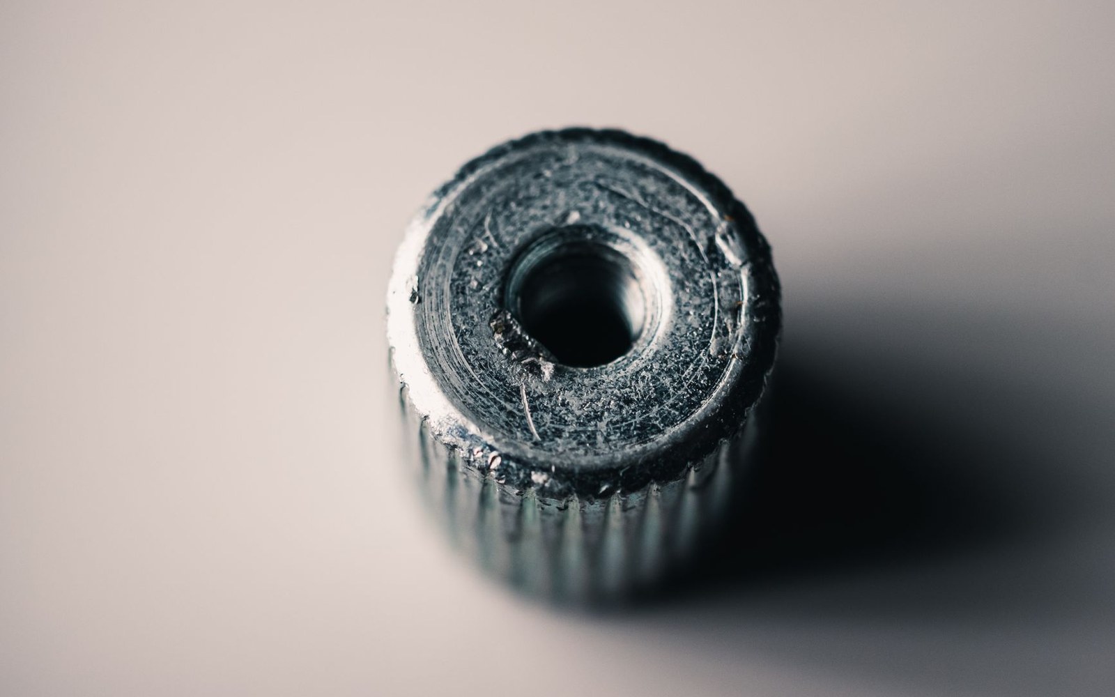 Close-up of a scratched metal knurled nut with a central hole on a plain background